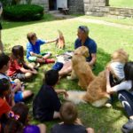 Group of campers sitting with Tom Richards and two of Nellie's dogs